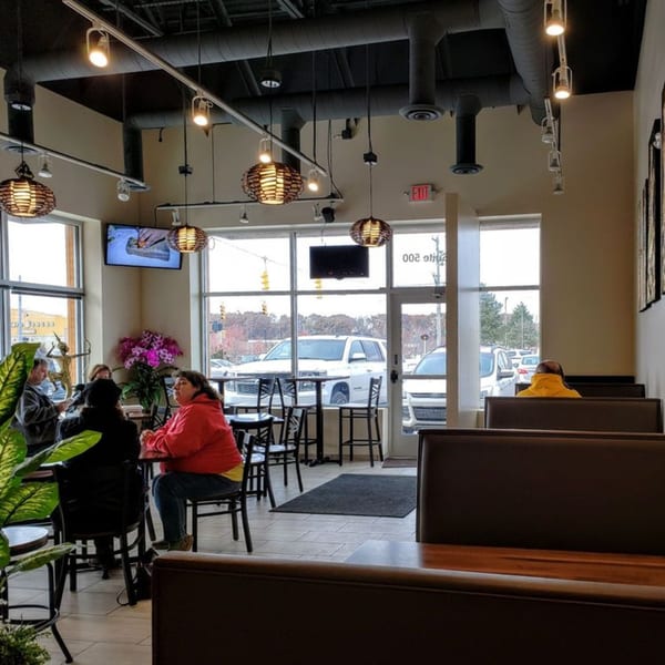 Diners seated at tables and booths inside Thai House Bistro, with large windows overlooking a parking lot.