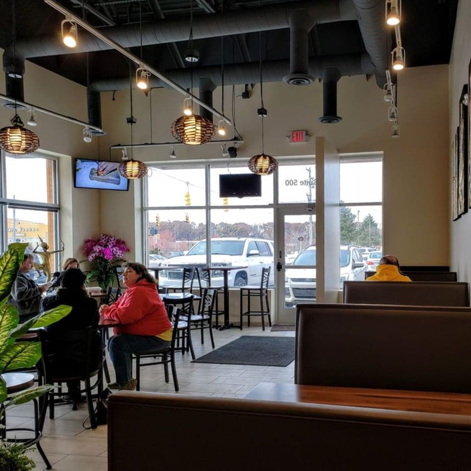 Diners seated at tables and booths inside Thai House Bistro, with large windows overlooking a parking lot.
