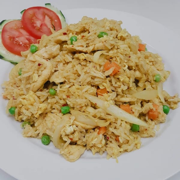 Chicken fried rice with peas, carrots, onions, and sliced tomatoes and cucumbers on a white plate.