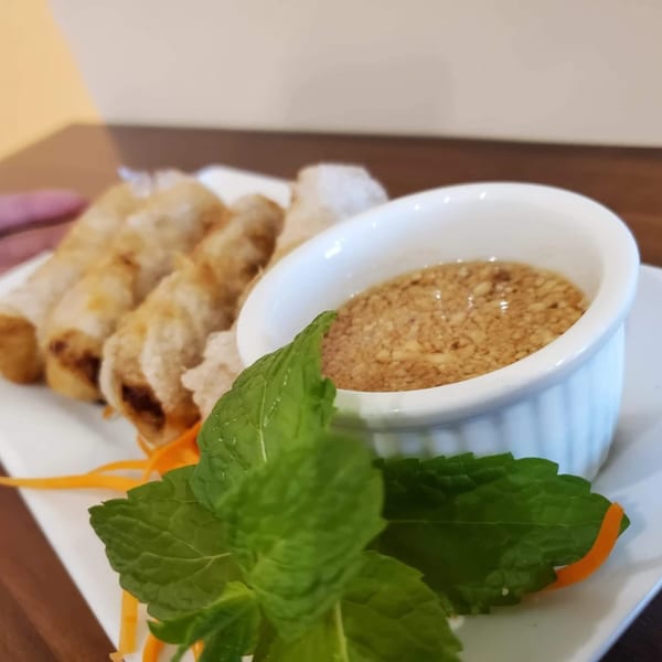 Crispy Thai spring rolls with a side of peanut dipping sauce, garnished with fresh mint and carrot.
