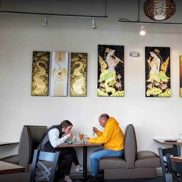 Two diners eating at a booth in Thai House Bistro, with traditional Thai art on the wall.